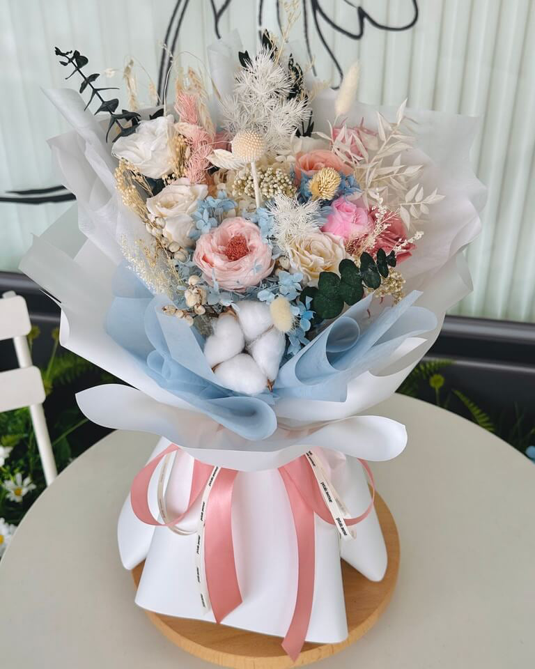 Handheld bouquet of blue and pink everlasting flowers with a natural, dried texture.