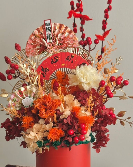 Decorative floral arrangement with red vase, fan, and lanterns on a neutral background