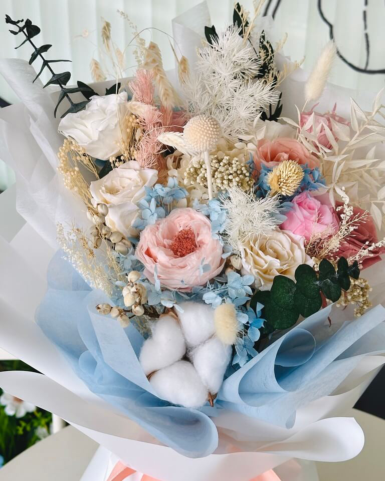 Colorful bouquet featuring preserved blue and pink everlasting flowers with green foliage.