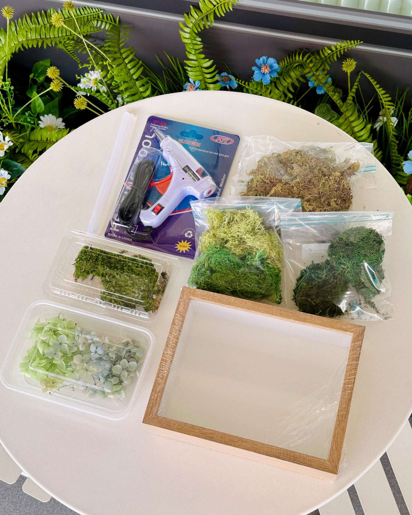 Complete DIY shadow box kit with oak-colored frame, preserved moss, artificial moss grasses, hydrangea bunches, and brown bottom sheet.