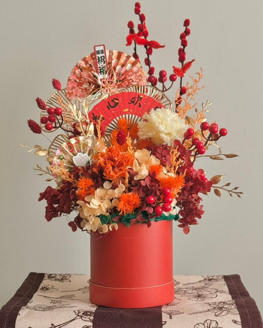 Decorative floral arrangement in a red bloom box with festive elements on a neutral background