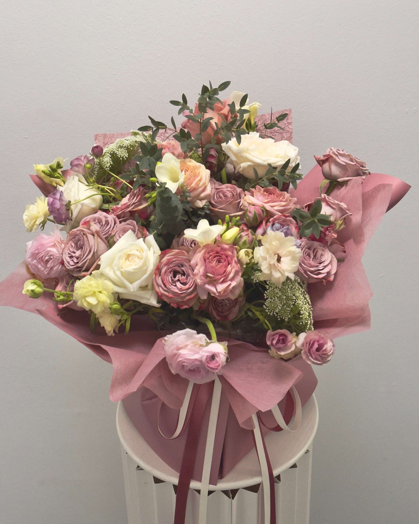Bouquet of flowers wrapped in pink paper on a white stand against a gray background