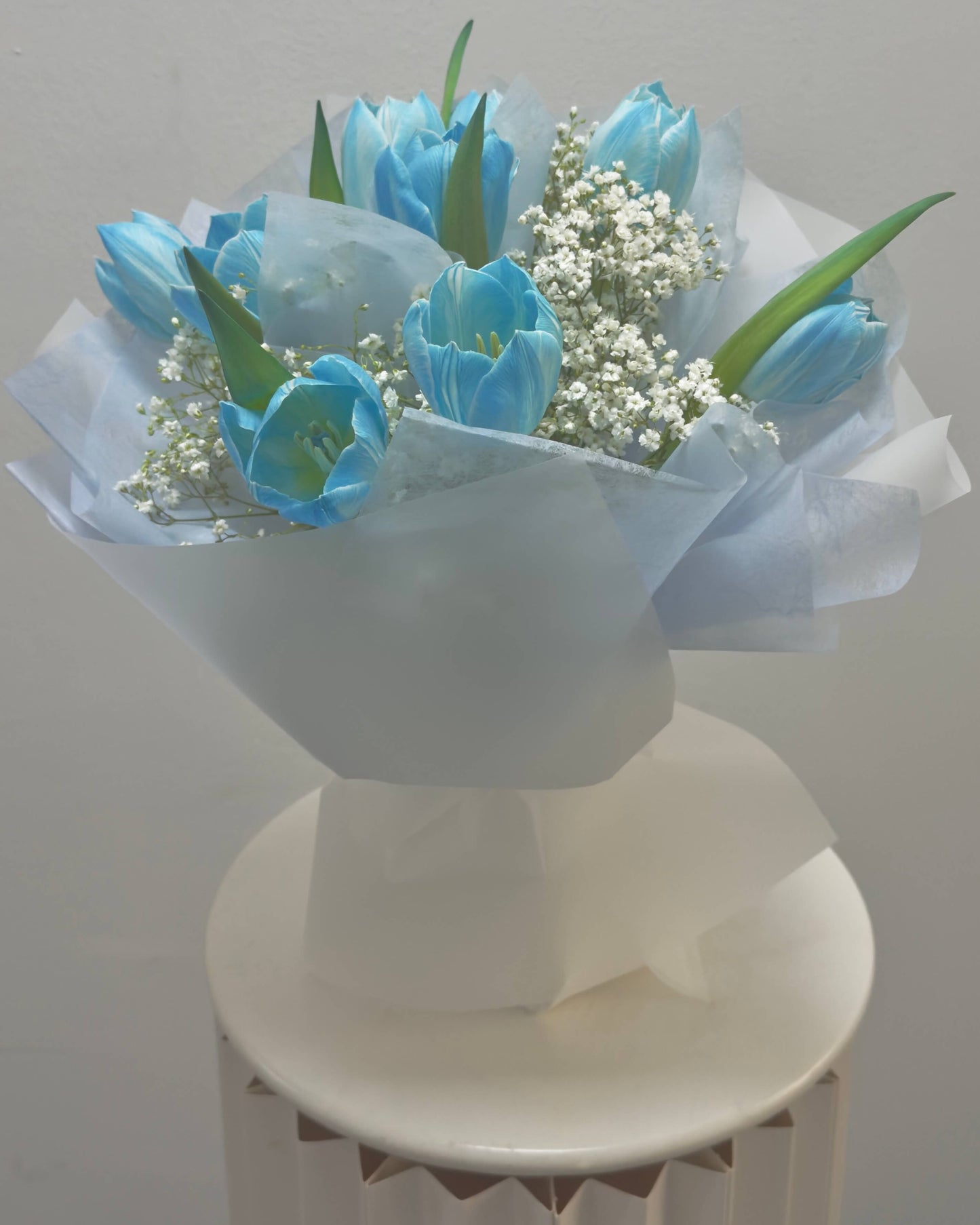 Bouquet of blue tulips with baby's breath on a white pedestal against a light gray background