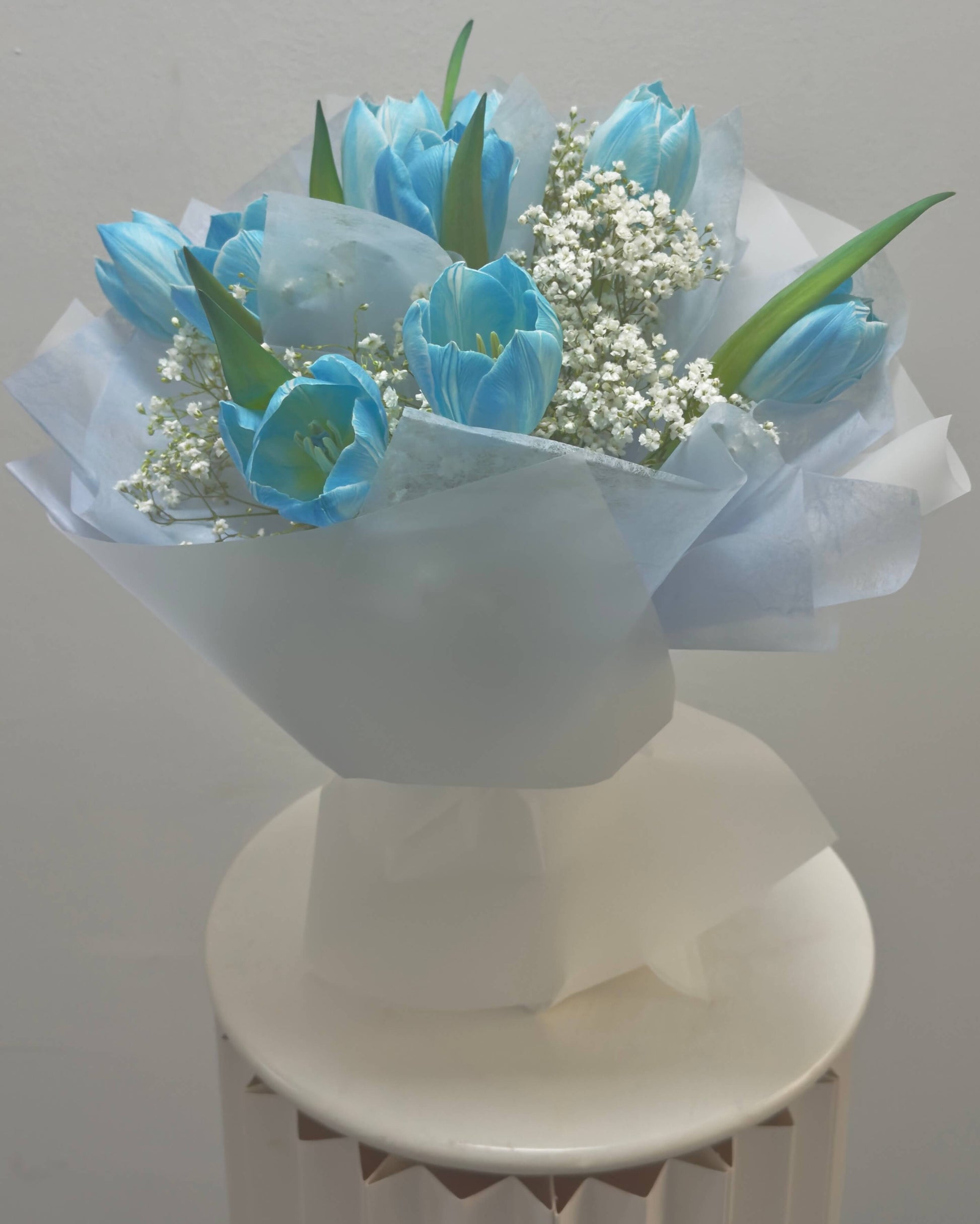Bouquet of blue tulips with baby's breath on a white pedestal against a light gray background