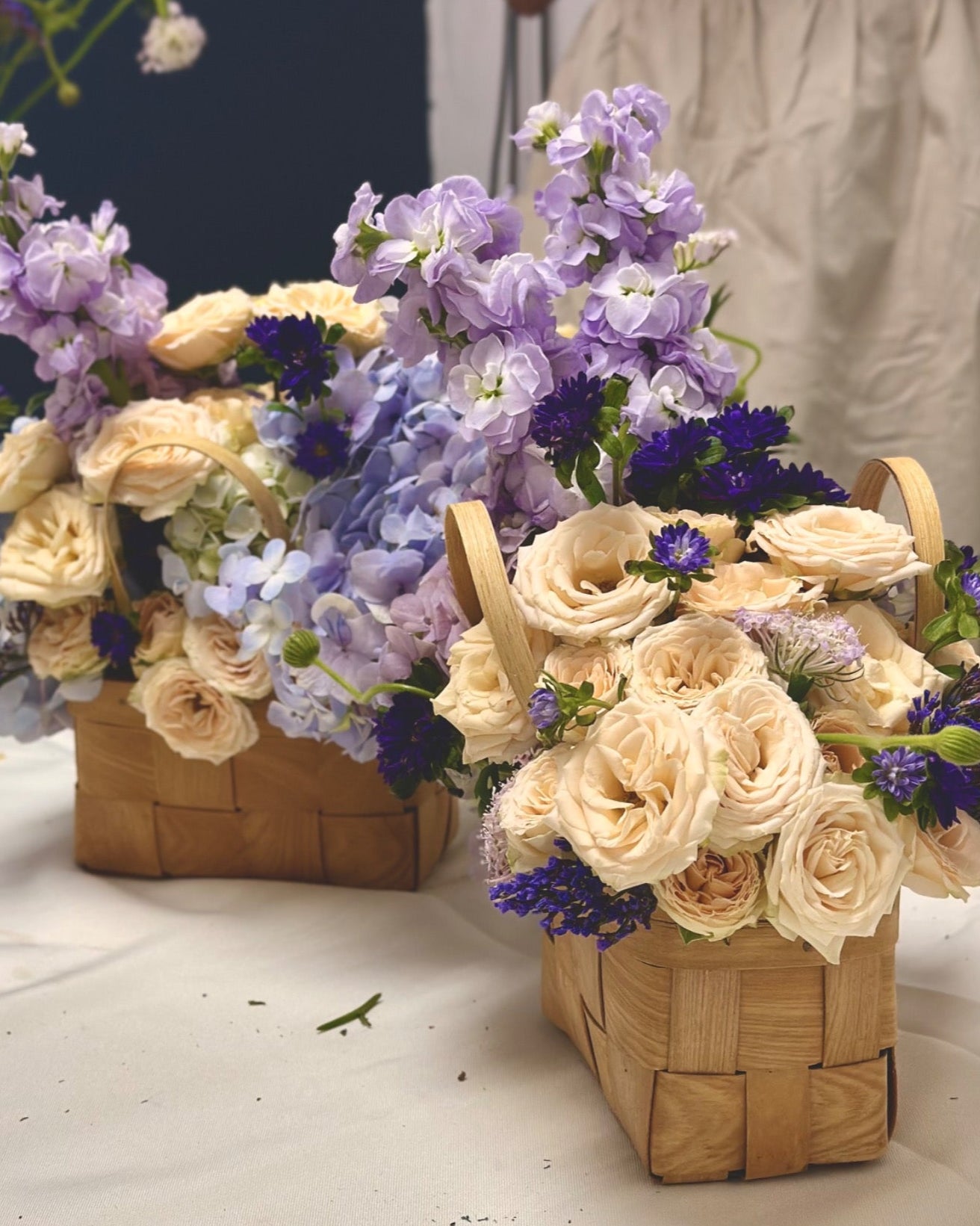 Two flower arrangements in woven baskets on a white surface. 
