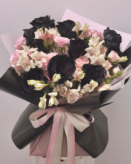 Bouquet of black, pink, and white flowers with ribbons on a light gray background