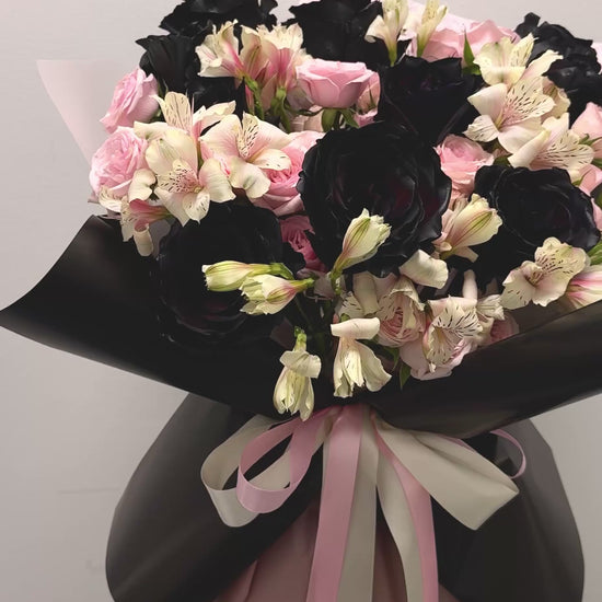 closeup video of bouquet. showing the deep black tinted roses, soft pink spray roses and white flowers a black and pink beauty