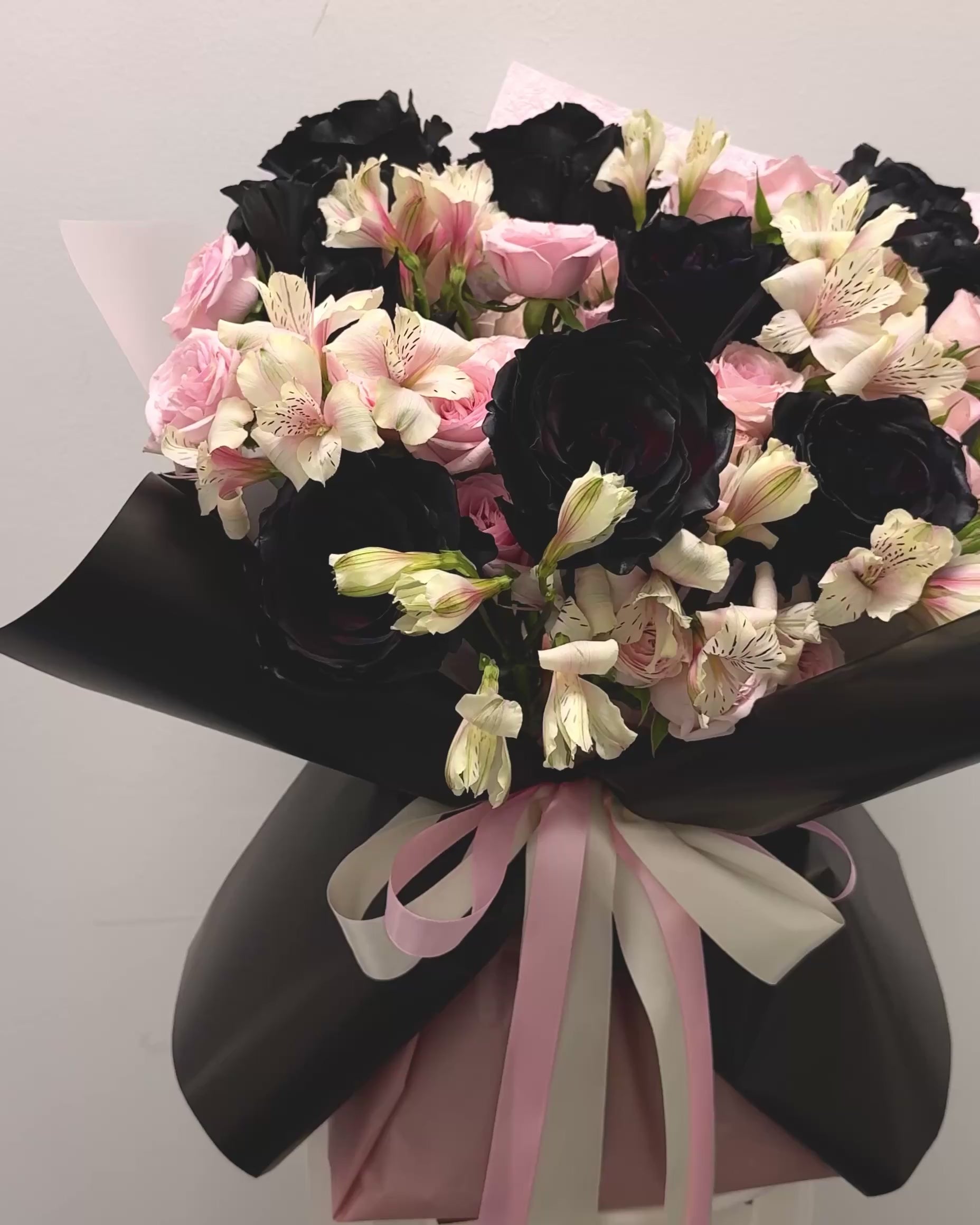 closeup video of bouquet. showing the deep black tinted roses, soft pink spray roses and white flowers a black and pink beauty